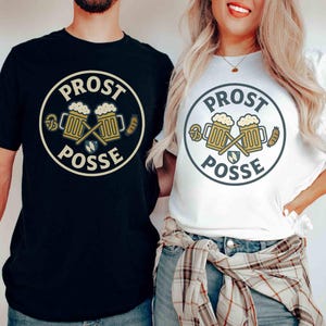 May include: Black and white t-shirts with a circular graphic that reads "PROST POSSE." The design includes two beer steins, pretzels, and sausages. The shirts are worn by two people. The text "each shirt sold separately" is at the bottom.
