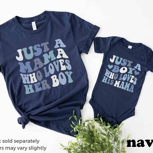 May include: Two navy blue shirts with a retro-style graphic design. The larger shirt says "Just a Mama Who Loves Her Boy" and the smaller shirt says "Just a Boy Who Loves His Mama".