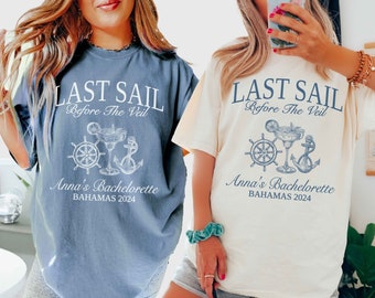 May include: Two t-shirts with the text "Last Sail Before The Veil" and "Anna's Bachelorette Bahamas 2024". The shirts are in blue jean and ivory colors. The design features a nautical theme with a steering wheel, anchor, and a margarita glass.