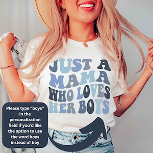 May include: White t-shirt with blue and gray text that reads "Just a Mama Who Loves Her Boys".