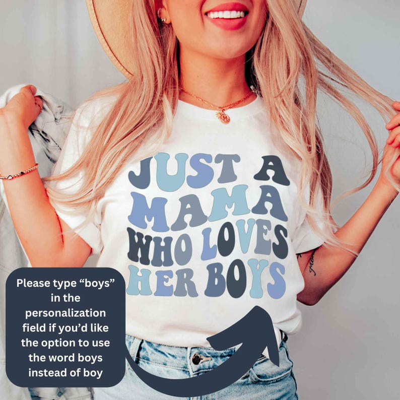 May include: White t-shirt with blue and gray text that reads "Just a Mama Who Loves Her Boys".