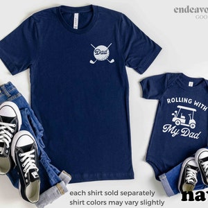 May include: Matching navy blue t-shirts for a father and child. The father's shirt has a white golf ball with crossed golf clubs and the word "Dad". The child's shirt has a white golf cart with the text "Rolling with My Dad".