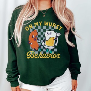 May include: Green sweatshirt with a white checkered background and a cartoon sausage and beer mug with the text "On My Wurst Behavior".