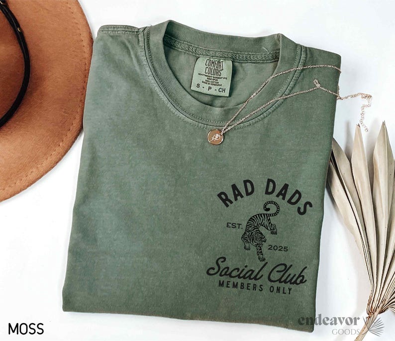 May include: A green t-shirt with a black graphic print of a tiger with the text "Rad Dads Social Club Members Only" and the text "Est. 2025".