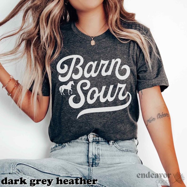 May include: A dark grey heather t-shirt with the text "Barn Sour" in white cursive lettering. A small white silhouette of a horse is to the left of the text.