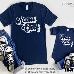 K&ouml;nnte beinhalten: Zwei marineblaue T-Shirts mit wei&szlig;em Retro-Text. Das gr&ouml;&szlig;ere Shirt sagt "Chefkoch" und das kleinere Shirt sagt "Sous Chef".