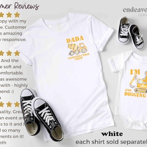 May include: White t-shirts and a baby onesie with construction-themed graphics. One shirt says "DADA CONSTRUCTION CREW" and the onesie says "I'M AND DIGGING IT" with a number 1. Black and white trainers are also in the image.