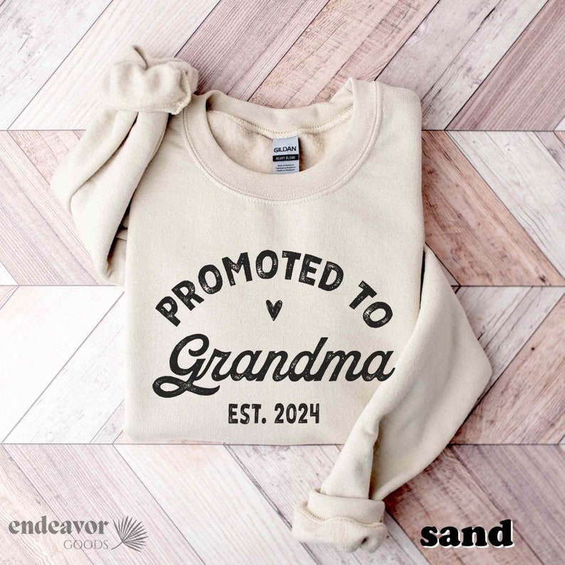 May include: A beige sweatshirt with the text "Promoted to Grandma Est. 2024" in black lettering.