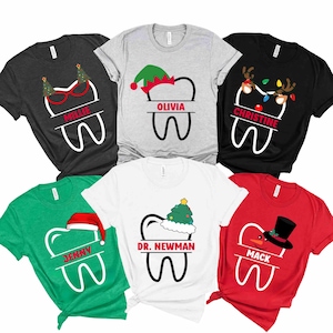 以下が含まれることがあります： クリスマスをテーマにしたTシャツのコレクション。歯の形をしたデザインに、お祝いの要素が加えられています。各シャツには「Millie」、「Olivia」、「Christine」などの名前が書かれています。シャツは黒、グレー、緑、白、赤など、さまざまな色があります。