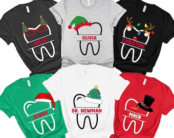 May include: A collection of Christmas-themed t-shirts featuring a tooth design with festive elements. Each shirt has a name, such as "Millie," "Olivia," and "Christine." The shirts come in various colors, including black, gray, green, white, and red.