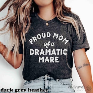 May include: A dark grey heather t-shirt with the text "Proud Mom of a Dramatic Mare" printed in white.
