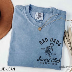 May include: A blue jean t-shirt with a black graphic of a tiger and the text "Rad Dads Social Club Members Only" with the text "Est. 2025" below the tiger.
