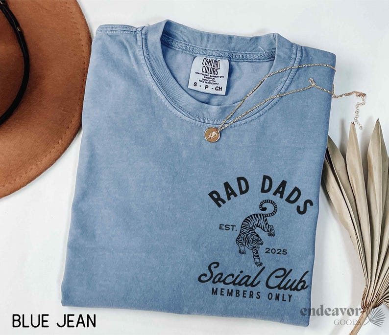 May include: A blue jean t-shirt with a black graphic of a tiger and the text "Rad Dads Social Club Members Only" with the text "Est. 2025" below the tiger.