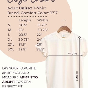K&ouml;nnte beinhalten: Cremefarbenes Unisex-T-Shirt f&uuml;r Erwachsene, das an einem Holzb&uuml;gel h&auml;ngt. Das Bild enth&auml;lt eine Gr&ouml;&szlig;entabelle mit Ma&szlig;en in Zoll f&uuml;r die Gr&ouml;&szlig;en S bis 3XL. Der Text lautet: "Legen Sie Ihr Lieblingshemd flach hin und messen Sie von Achsel zu Achsel, um die perfekte Passform zu erhalten."