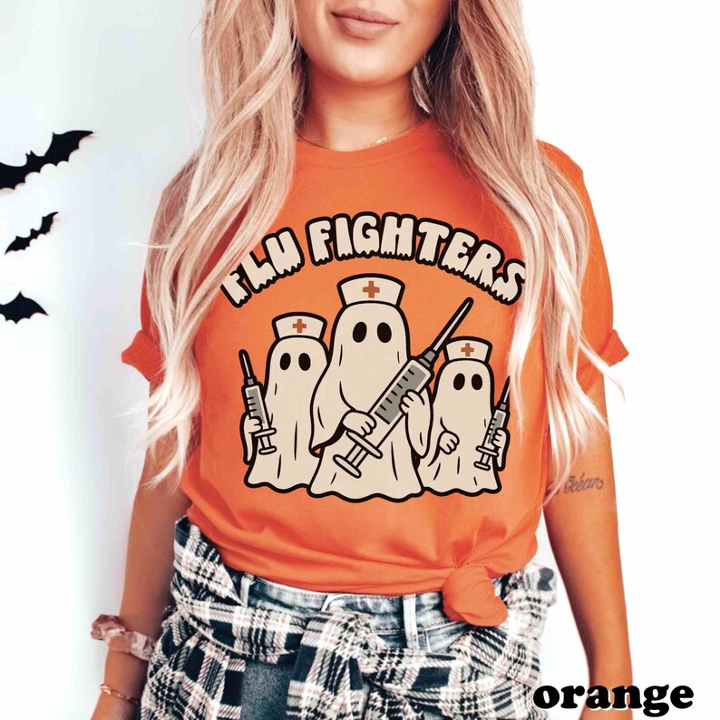 May include: An orange t-shirt featuring the words "FLU FIGHTERS" above a graphic of three ghost figures dressed as nurses, each holding a syringe. The tee is a solid orange colour.