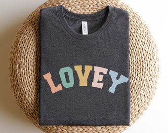 May include: A dark gray t-shirt with the word "LOVEY" printed in rainbow colors in a retro font.