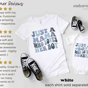 May include: Two white t-shirts with blue and gray text. The larger shirt says "Just a Mama Who Loves Her Boy". The smaller shirt says "Just a Boy Who Loves His Mama". Both shirts are on a white background with a pair of black sneakers.