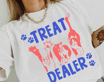 May include: White t-shirt with a blue and red cat-themed graphic. The text "TREAT DEALER" is in blue, with red cat illustrations and paw prints. The word "white" is printed at the bottom left of the shirt.