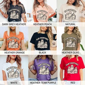 May include: A selection of t-shirts in diverse colours, each displaying the text "FLU FIGHTERS" above a graphic of three ghost-like figures wearing nurse hats and holding syringes. Colours include dark grey, peach, natural, orange, black, olive, white, purple, and red.