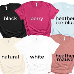 May include: Six t-shirts in different colors, including black, berry, heather ice blue, natural, white, and heather mauve. Each shirt has a different color name printed on the front.
