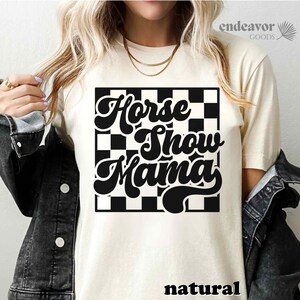 K&ouml;nnte beinhalten: Ein wei&szlig;es T-Shirt mit einem schwarz-wei&szlig; karierten Hintergrund und dem Text "Horse Show Mama" in einer Retro-Schrift.