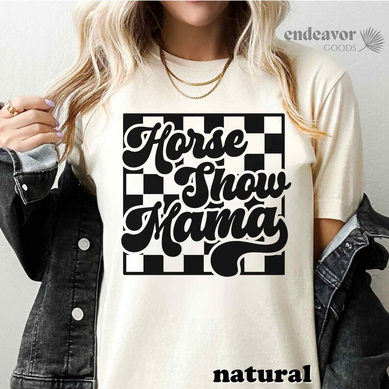K&ouml;nnte beinhalten: Ein wei&szlig;es T-Shirt mit einem schwarz-wei&szlig; karierten Hintergrund und dem Text "Horse Show Mama" in einer Retro-Schrift.