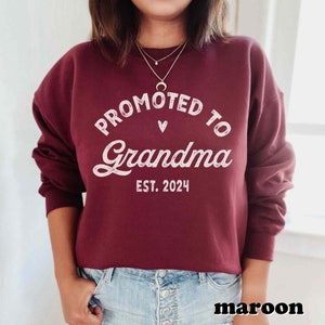 May include: Maroon sweatshirt with the text "Promoted to Grandma Est. 2024" in white lettering.