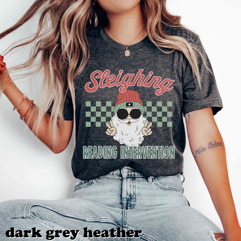 K&ouml;nnte beinhalten: Ein dunkelgraues Heather-T-Shirt mit einer Retro-Grafik eines Weihnachtsmanns mit Sonnenbrille und M&uuml;tze. Die Grafik lautet "Sleighing Reading Intervention".