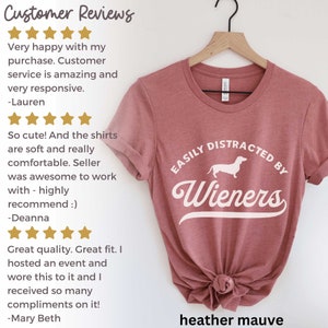 Peut inclure: T-shirt en mauve heather avec une silhouette de teckel blanche et le texte "EASILY DISTRACTED BY WIENERS" dans une police blanche de style vintage. Des commentaires clients sont inclus sur le c&ocirc;t&eacute; gauche de l'image.
