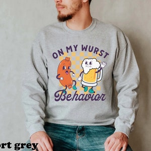 May include: A gray sweatshirt with a cartoon sausage and beer design. The text on the sweatshirt reads "On My Wurst Behavior".