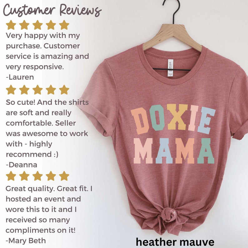 May include: Heather mauve t-shirt with the text "DOXIE MAMA" in colorful block letters. The shirt is displayed on a hanger. Customer reviews are visible on the left side of the image.