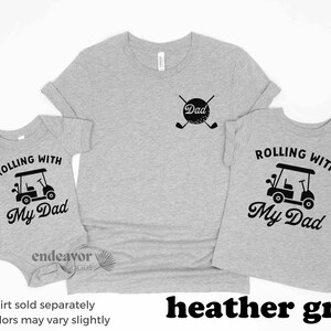 May include: Three heather grey t-shirts with a golf cart and the text "Rolling with My Dad". The adult shirt has the text "Dad" and a golf ball with crossed golf clubs.