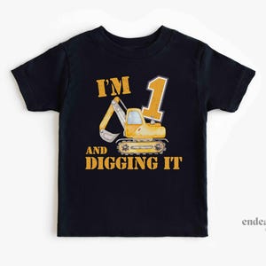 May include: Black toddler t-shirt featuring a yellow excavator graphic and the text "I'M 1 AND DIGGING IT". The design includes a large number 1 and a cartoon excavator.