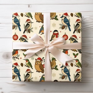 May include: A wrapped gift with a cream-colored paper featuring a repeating pattern of various birds wearing Santa hats, with pinecones, ornaments, and snowflakes. The gift is tied with a light pink satin ribbon and bow, set against a white wooden background.