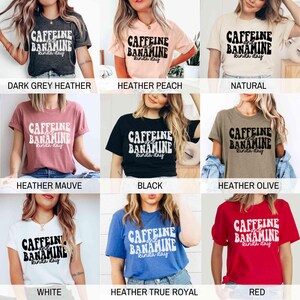 May include: A selection of short-sleeved t-shirts in diverse colours, each displaying the text "CAFFEINE and BANAMINE kinda day" in a bold, retro font. Colours include dark grey, peach, natural, mauve, black, olive, white, blue, and red.