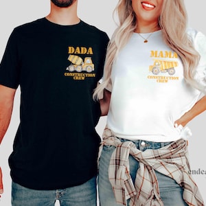 May include: Matching black and white t-shirts with construction-themed graphics. The black shirt says "DADA CONSTRUCTION CREW" with a yellow cement mixer. The white shirt says "MAMA CONSTRUCTION CREW" with a yellow dump truck.