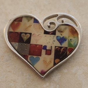Könnte beinhalten: Ein silberner herzförmiger Anhänger mit einem bunten Mosaik aus Herzen im Inneren. Der Anhänger hat oben ein dekoratives Wirbeldesign.