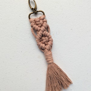 May include: A pink macrame keychain with a brass key ring and a tassel.