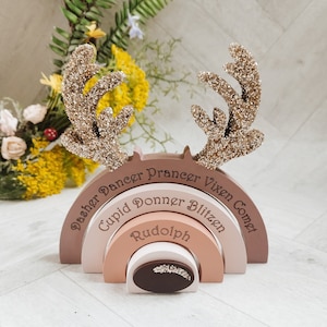 May include: A wooden reindeer antler arch with five rainbow-coloured arches, each with a different reindeer name: Dasher, Dancer, Prancer, Vixen, Comet, Cupid, Donner, Blitzen, and Rudolph.