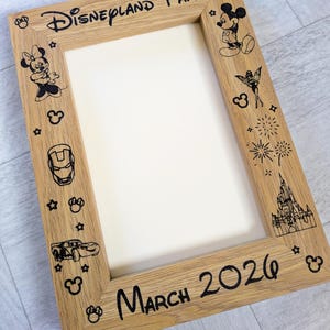 May include: Wooden picture frame with the words "Disneyland Paris" and "March 2026" in black. The frame is decorated with black illustrations of Disney characters, stars, and fireworks.