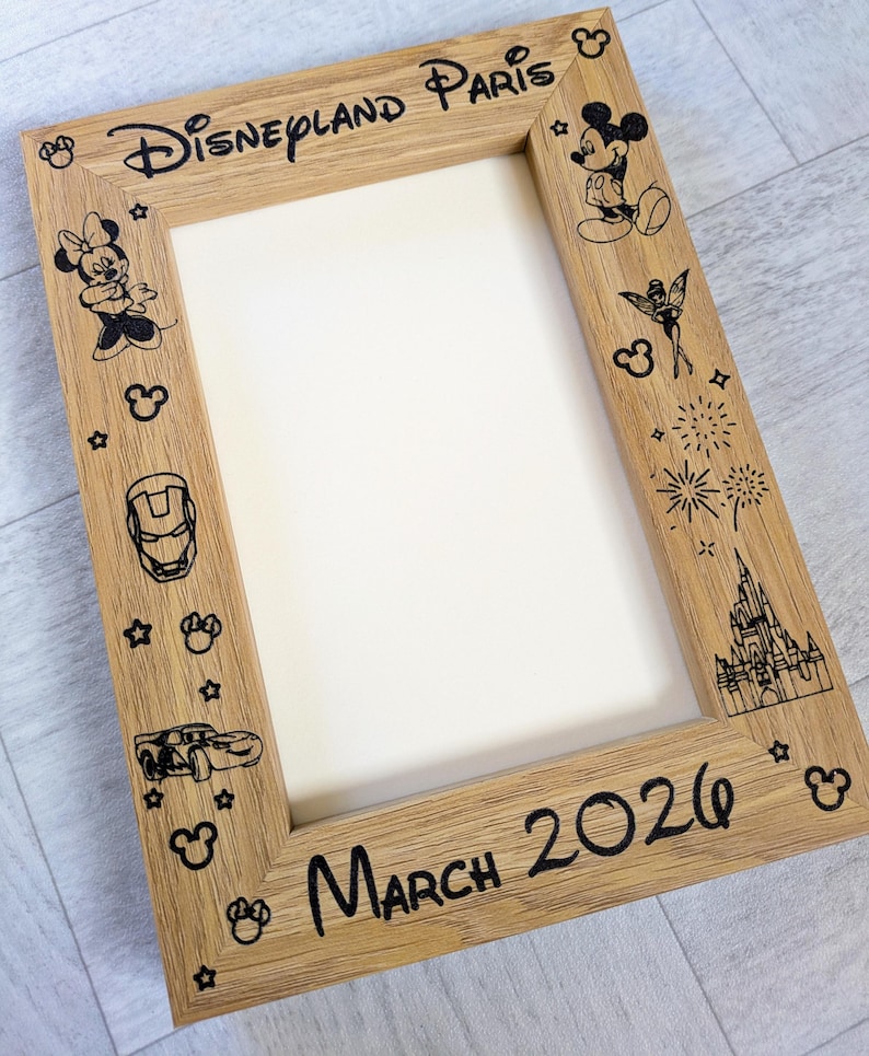 May include: Wooden picture frame with the words "Disneyland Paris" and "March 2026" in black. The frame is decorated with black illustrations of Disney characters, stars, and fireworks.