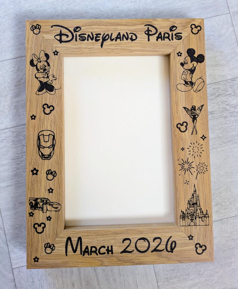 May include: Wooden picture frame with the words "Disneyland Paris" and "March 2026" etched in black. The frame is decorated with cartoon characters and icons, including Mickey and Minnie Mouse, and a castle.