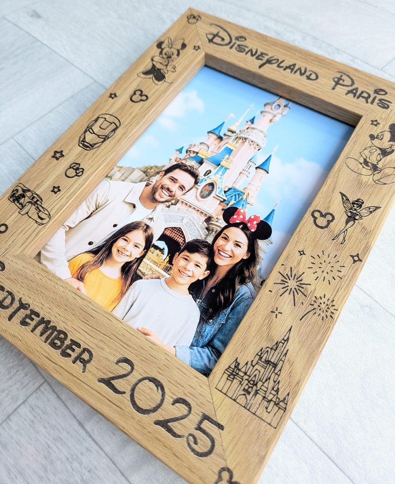 May include: Wooden photo frame with a family portrait in front of a castle. The frame is engraved with Disney-themed illustrations and the text "Disneyland Paris" and "September 2025". The frame has a light brown color.