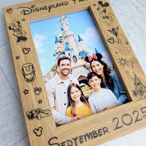 May include: Wooden photo frame with the text "Disneyland Paris" and "September 2025". The frame features etched Disney character designs and holds a family photo in front of a castle.