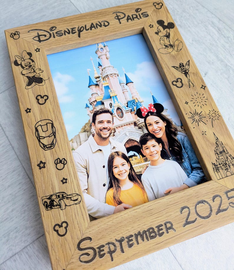 May include: Wooden photo frame with the text "Disneyland Paris" and "September 2025". The frame features etched Disney character designs and holds a family photo in front of a castle.
