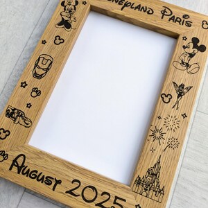 May include: Wooden picture frame with the words "Disneyland Paris" and "August 2025" etched into the wood. The frame is decorated with Disney character illustrations, including Mickey and Minnie Mouse, and other Disney-themed icons.