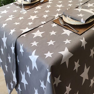 May include: A grey tablecloth with a white star pattern. The tablecloth is set for a dinner with two place settings, including plates, cutlery, and napkins.