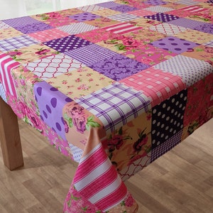 Op de afbeelding: Een patchwork tafelkleed in een roze, paarse en crème kleurschema. Het tafelkleed heeft een verscheidenheid aan patronen, waaronder stippen, strepen en bloemenmotieven.