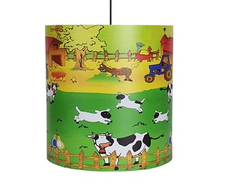 May include: A green and yellow cylindrical lampshade with a farm scene. The scene includes a blue tractor, a cow, chickens, and sheep. The lampshade is perfect for a child's room.