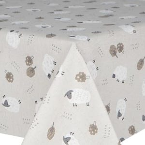 May include: A light beige tablecloth with a repeating pattern of white sheep with grey faces and legs. The design includes brown tree and leaf motifs, and small text elements. The fabric is folded, showing the pattern's continuity.